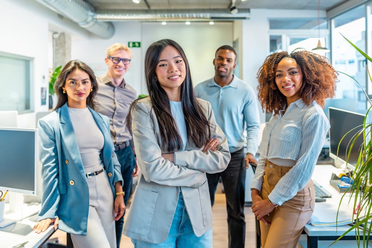 Diverse group of professionals smiling confidently in a modern coworking office, embodying teamwork and collaboration in a vibrant workspace