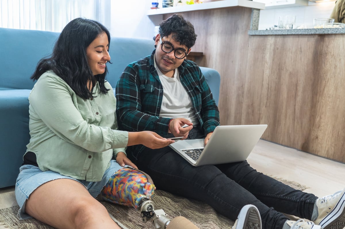 A couple at home looking at a laptop screen, the moment of decision before accessing a service — the pre-arrival accessibility moment