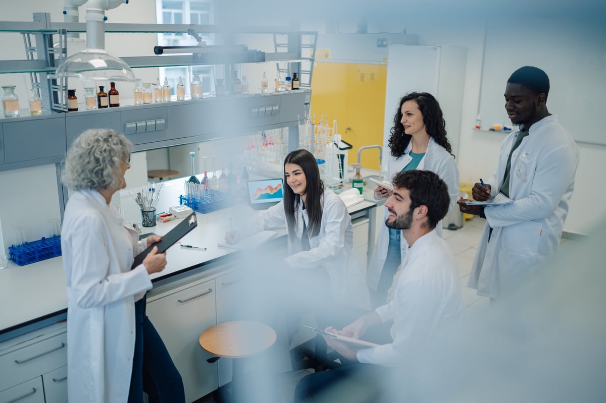 Group of diverse scientists and students wearing lab coats, collaborating in a modern research laboratory