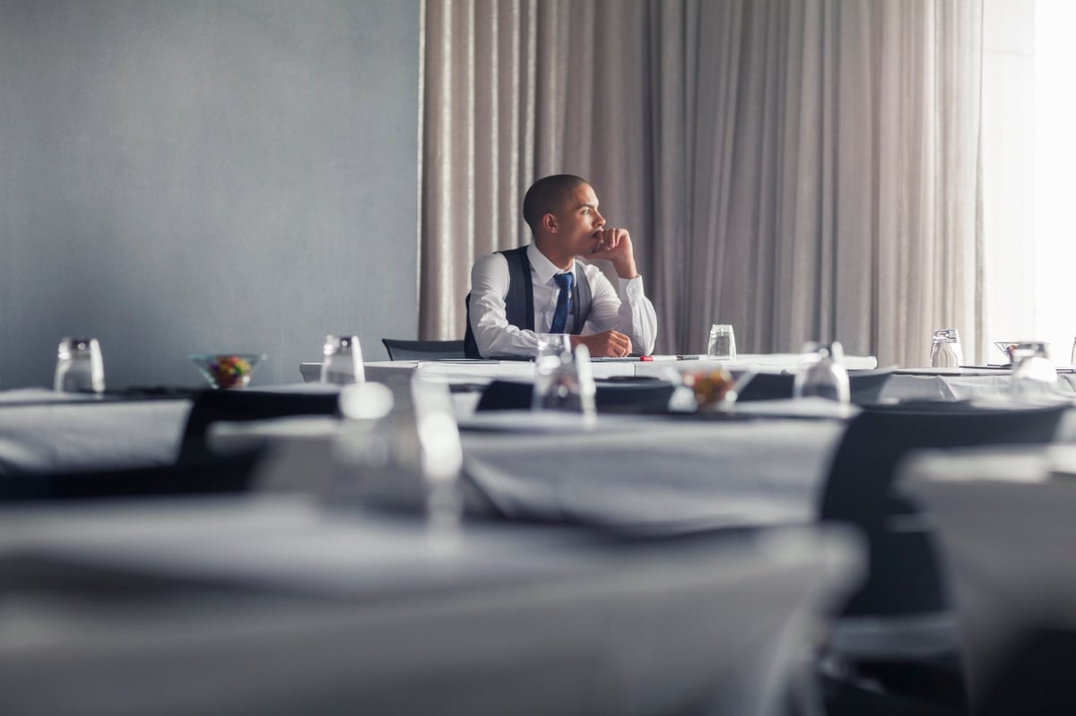 A person sitting alone at a conference table, lost in thought in an empty meeting room